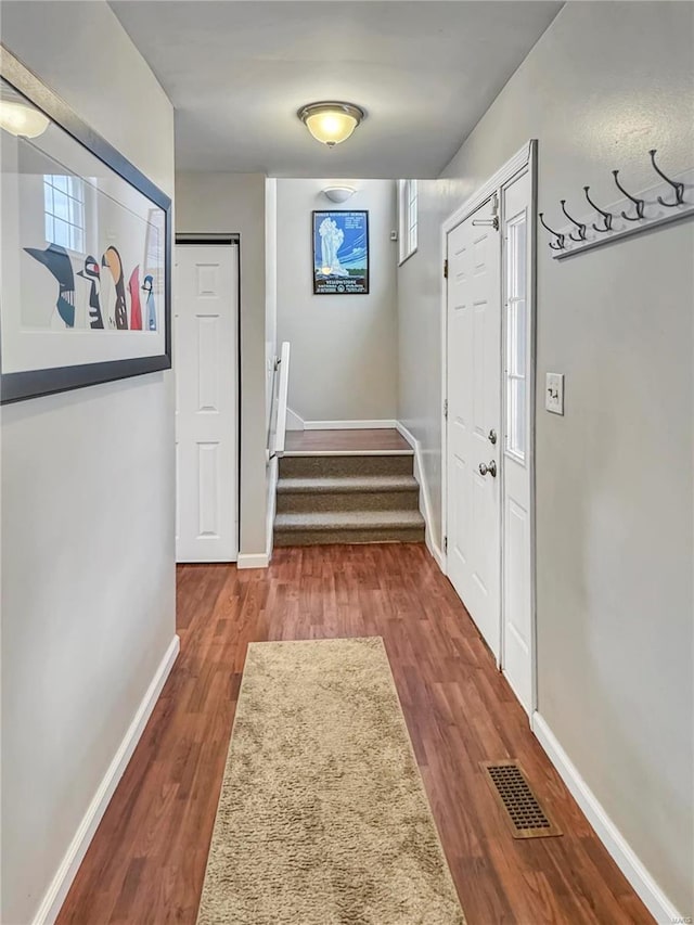 hallway featuring baseboards, stairs, visible vents, and wood finished floors