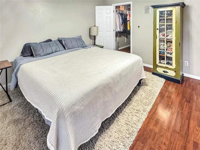 bedroom featuring a closet, a spacious closet, baseboards, and wood finished floors