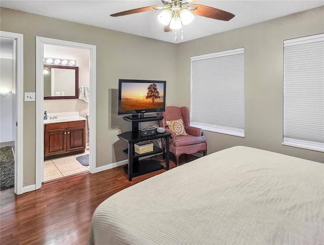 bedroom featuring ceiling fan, connected bathroom, a sink, baseboards, and dark wood finished floors