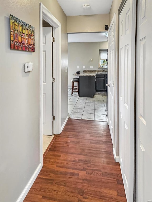 hallway with light wood-type flooring, a sink, and baseboards