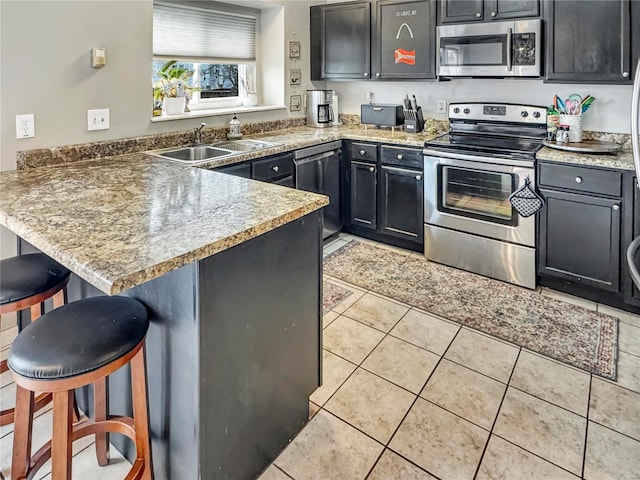 kitchen featuring light tile patterned floors, a breakfast bar area, stainless steel appliances, a peninsula, and a sink