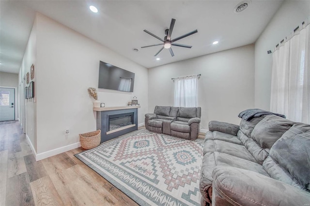 living area with light wood-style flooring, recessed lighting, visible vents, baseboards, and a glass covered fireplace