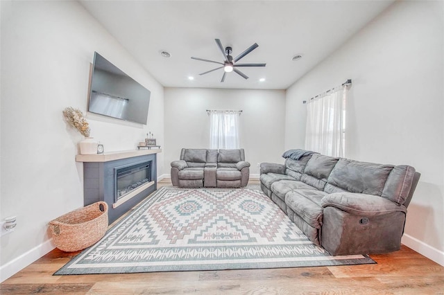 living room with a wealth of natural light, baseboards, wood finished floors, and a glass covered fireplace