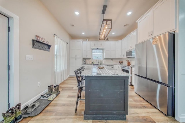 kitchen with stainless steel appliances, a kitchen island, white cabinetry, light stone countertops, and light wood finished floors