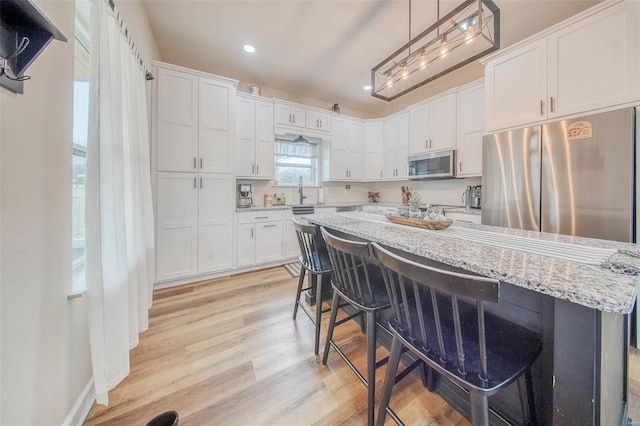 kitchen with white cabinets, stainless steel microwave, light wood-style flooring, and a kitchen breakfast bar