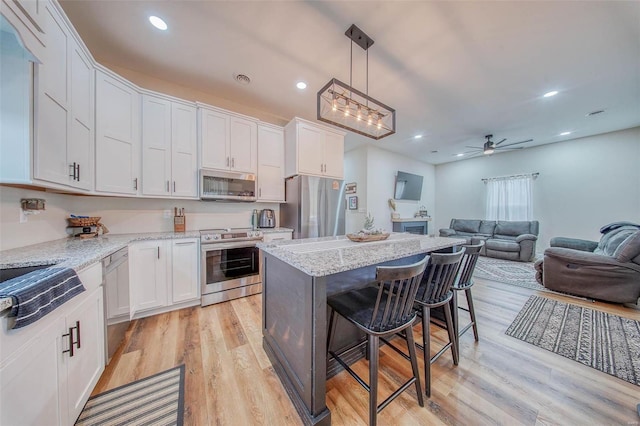 kitchen featuring light wood finished floors, white cabinetry, a kitchen bar, and appliances with stainless steel finishes