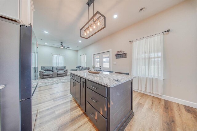 kitchen with light stone countertops, light wood-style flooring, white cabinetry, and pendant lighting