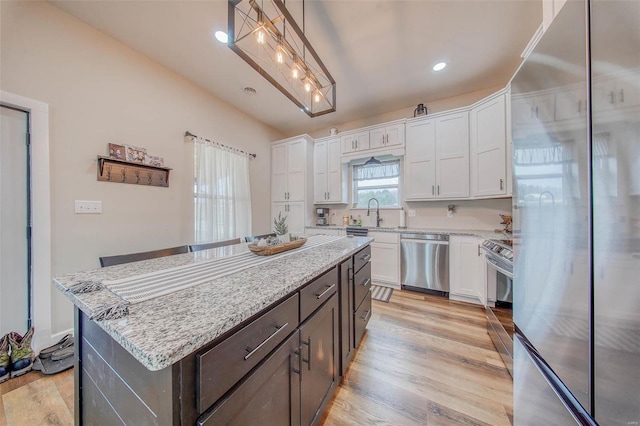 kitchen with a center island, appliances with stainless steel finishes, white cabinetry, light stone countertops, and light wood-type flooring