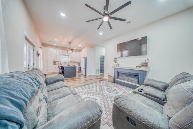 living room featuring recessed lighting, visible vents, a ceiling fan, a glass covered fireplace, and light wood-type flooring