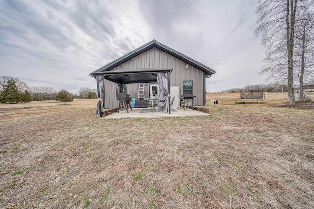 rear view of property with a trampoline, a patio, and a yard