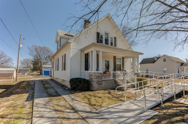 view of front of property featuring covered porch, a chimney, and an outdoor structure