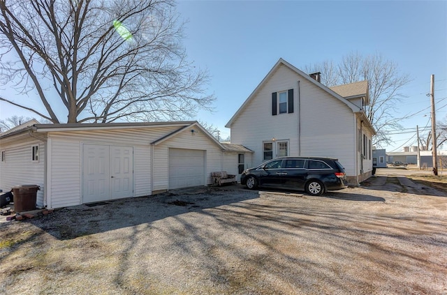 view of home's exterior with dirt driveway, a chimney, an outbuilding, and a detached garage