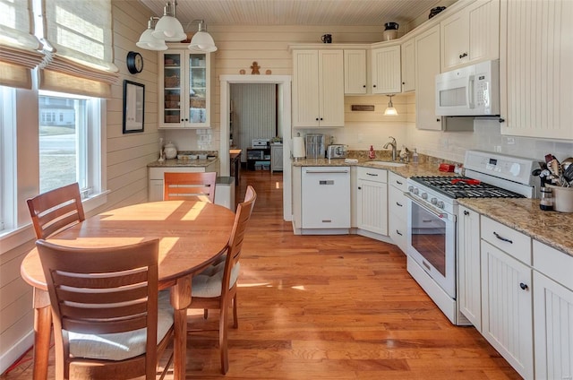 kitchen featuring light wood-style flooring, white appliances, a sink, backsplash, and glass insert cabinets