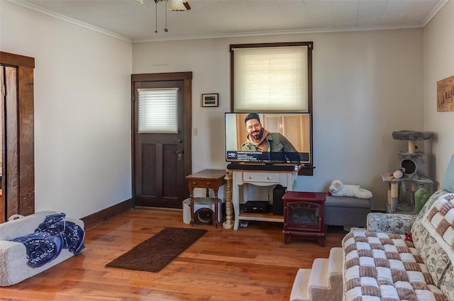 living room with ornamental molding, a ceiling fan, a wood stove, wood finished floors, and baseboards