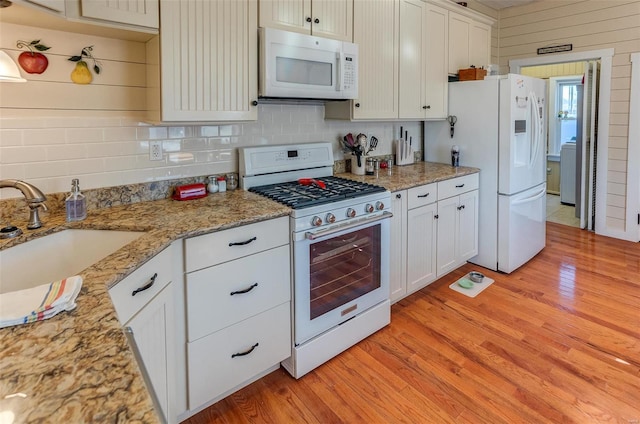 kitchen with light wood-style flooring, white appliances, a sink, white cabinetry, and backsplash