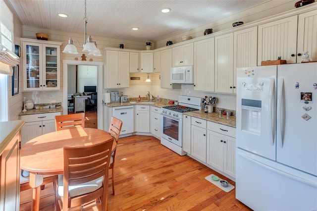 kitchen with white appliances, a sink, light wood finished floors, glass insert cabinets, and pendant lighting