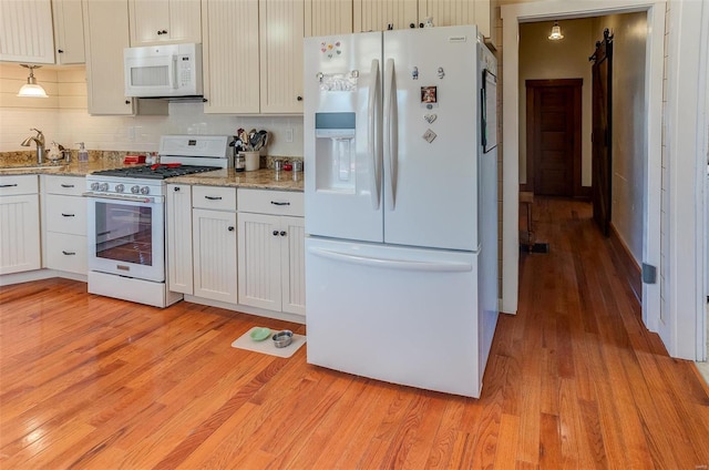 kitchen with light wood finished floors, tasteful backsplash, white cabinets, light stone countertops, and white appliances