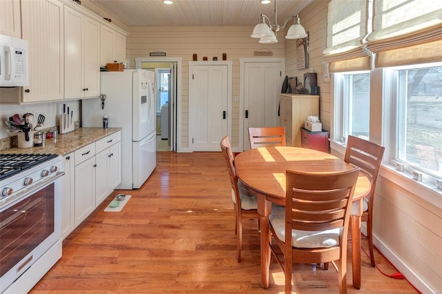 kitchen featuring pendant lighting, light wood-style flooring, white cabinets, wooden walls, and white appliances