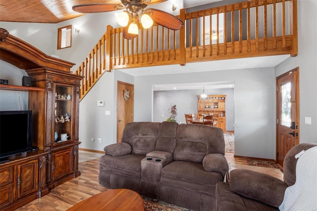 living area with wood finished floors, a towering ceiling, a ceiling fan, baseboards, and stairway