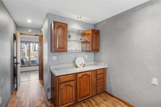 kitchen with brown cabinets, open shelves, light wood-style floors, light stone countertops, and baseboards