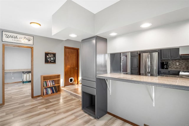 kitchen with black electric stovetop, tasteful backsplash, freestanding refrigerator, light wood-type flooring, and a kitchen bar