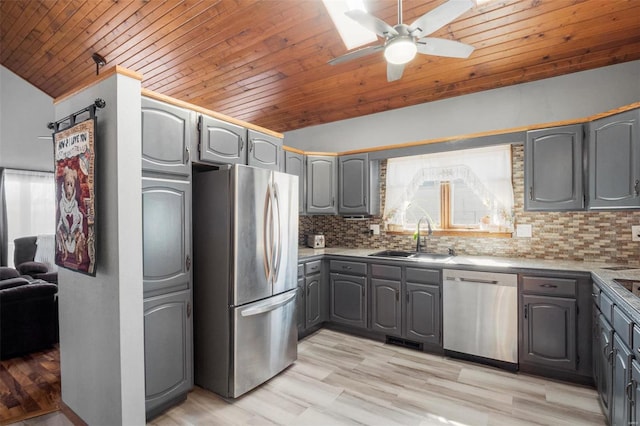 kitchen featuring tasteful backsplash, vaulted ceiling, gray cabinets, stainless steel appliances, and a sink