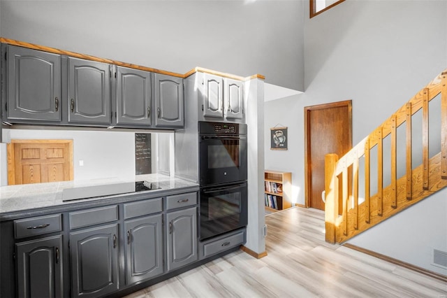 kitchen featuring baseboards, a high ceiling, gray cabinets, light wood-type flooring, and black appliances