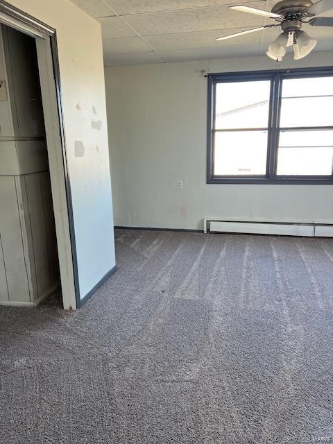 empty room with a baseboard heating unit, a paneled ceiling, ceiling fan, and carpet floors