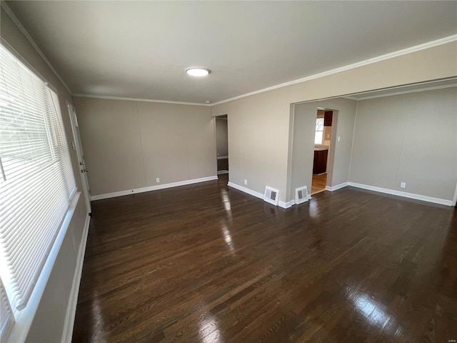 spare room featuring dark wood-style floors, ornamental molding, visible vents, and baseboards