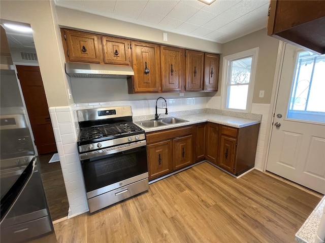 kitchen with stainless steel range with gas cooktop, brown cabinets, light wood-style floors, a sink, and under cabinet range hood