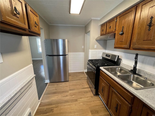 kitchen with light wood-style floors, stainless steel appliances, light countertops, under cabinet range hood, and a sink