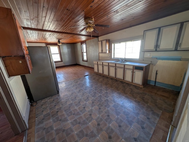 kitchen with light countertops, freestanding refrigerator, a sink, wooden ceiling, and baseboards