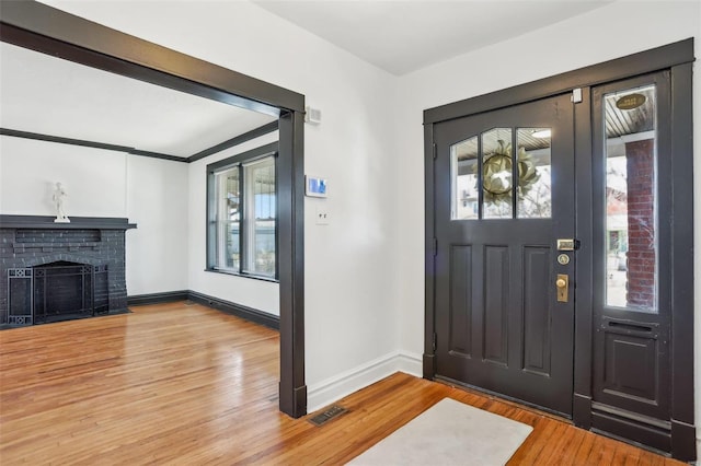 entryway with light wood finished floors, a fireplace, visible vents, and baseboards