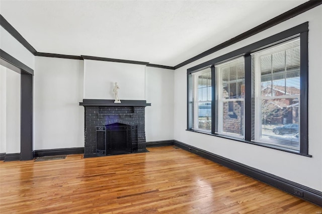 unfurnished living room featuring light wood finished floors, a brick fireplace, baseboards, and crown molding