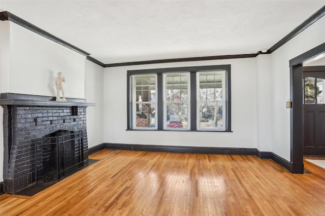 unfurnished living room with light wood-type flooring, a brick fireplace, baseboards, and crown molding