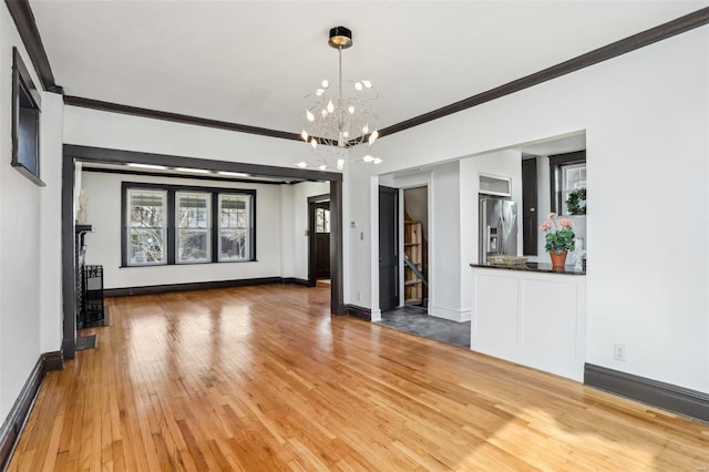 unfurnished living room with an inviting chandelier, wood-type flooring, ornamental molding, and baseboards