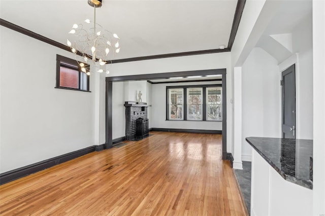 unfurnished living room with ornamental molding, light wood-style floors, a brick fireplace, a chandelier, and baseboards