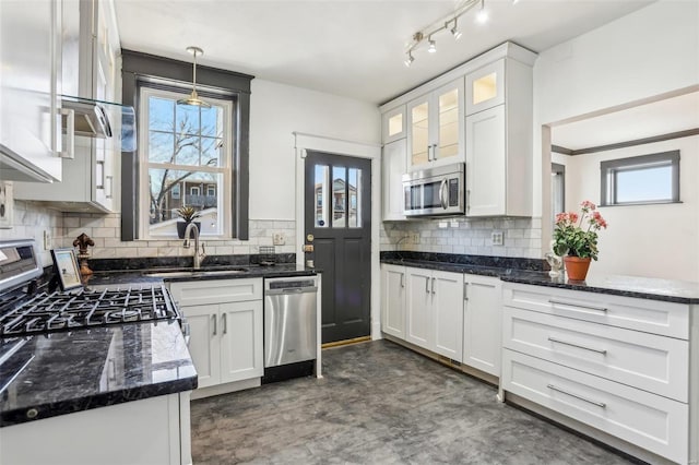 kitchen with a sink, white cabinets, appliances with stainless steel finishes, dark stone countertops, and glass insert cabinets