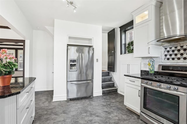 kitchen featuring tasteful backsplash, glass insert cabinets, stainless steel appliances, wall chimney range hood, and white cabinetry