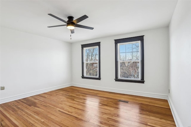 unfurnished room with a ceiling fan, visible vents, baseboards, and wood finished floors