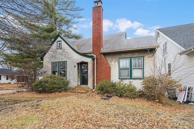 view of front facade featuring a shingled roof, a chimney, and stucco siding