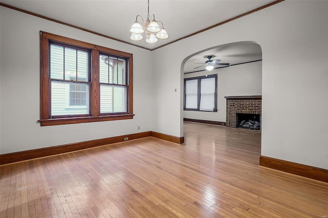 interior space featuring light wood-type flooring, a brick fireplace, arched walkways, and crown molding