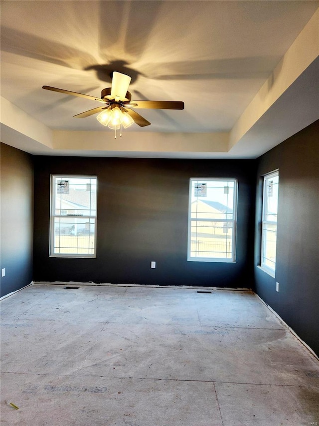 unfurnished room featuring concrete flooring, a raised ceiling, and a ceiling fan