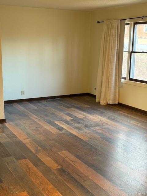 empty room with baseboards and dark wood-type flooring