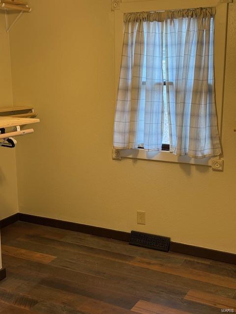 unfurnished room with dark wood-type flooring, visible vents, and baseboards