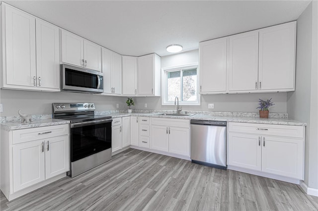 kitchen featuring white cabinets, stainless steel appliances, a textured ceiling, light wood-style floors, and a sink