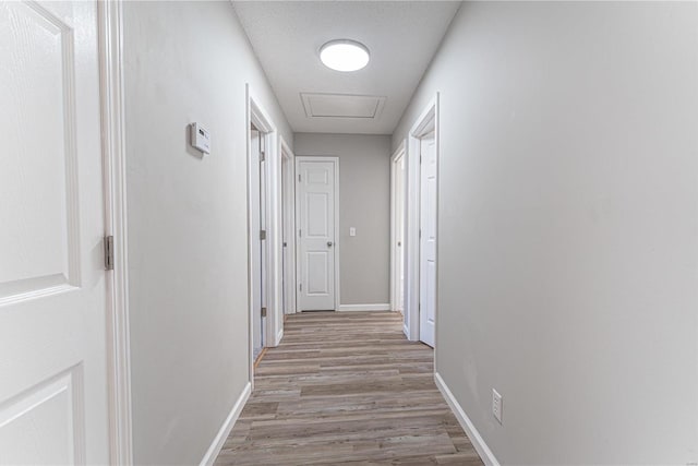 corridor with light wood-style floors, attic access, baseboards, and a textured ceiling