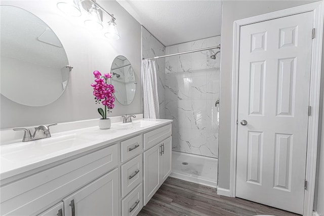 bathroom featuring a textured ceiling, a marble finish shower, a sink, and wood finished floors