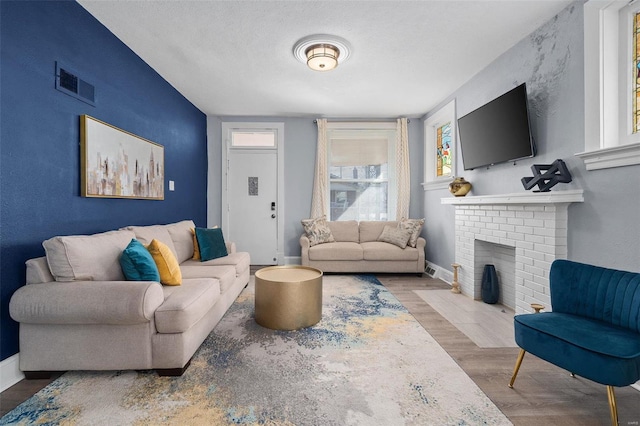 living room featuring baseboards, visible vents, wood finished floors, a textured ceiling, and a fireplace