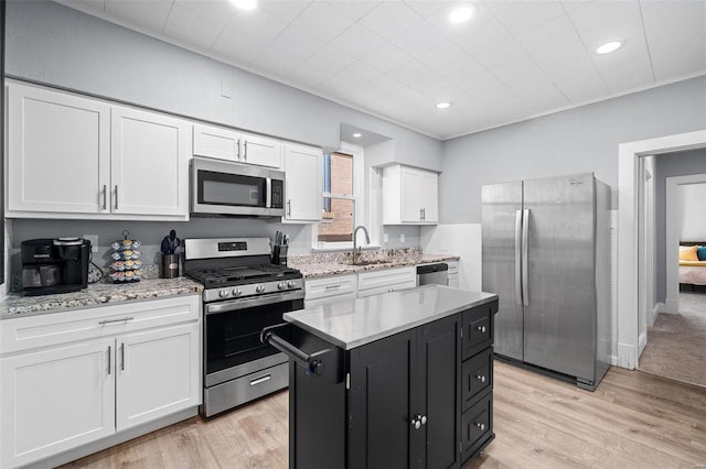 kitchen with stainless steel appliances, white cabinets, light wood-style flooring, and dark cabinets